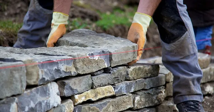 Mason setting a course of natural stone by hand